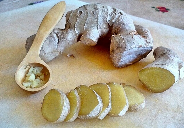 raíz de jengibre en cachitos junto a una cucharita de madera