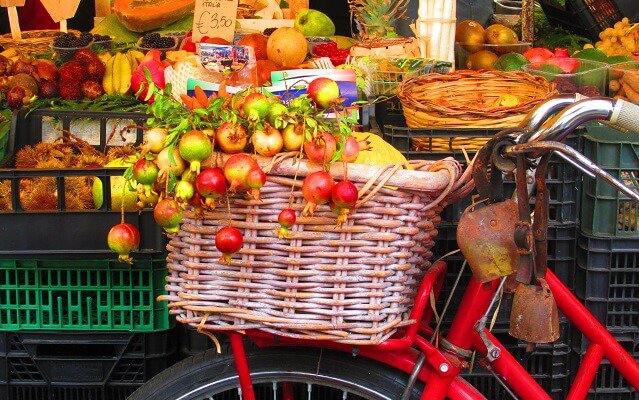 una bicicleta repleta de verduras al lado de una fruteria