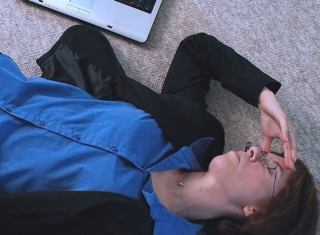 mujer tumbada en el suelo junto a un ordenador portatil