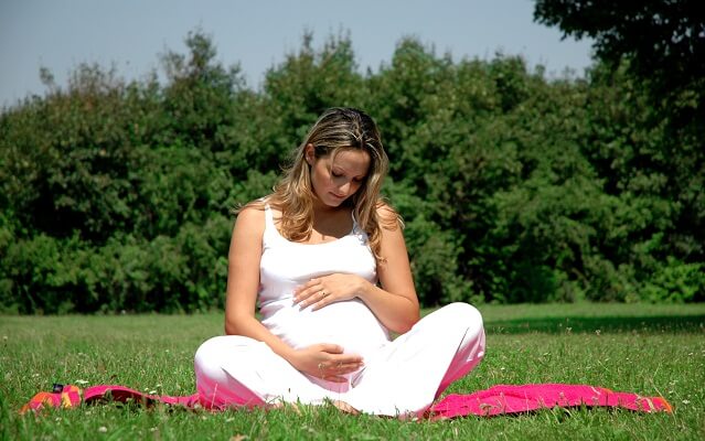 mujer embarazada sentada en el cesped de un parque