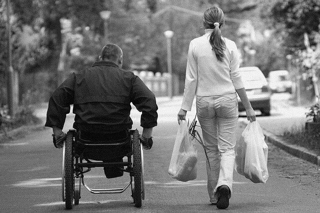 hombre en silla de ruedas junto a mujer que lleva unas bolsas