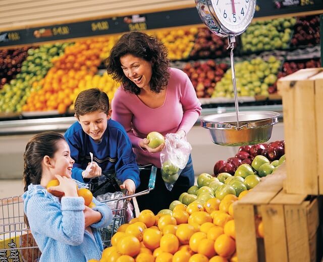 una madre con sus dos hijos al lado de las frutas de un supermercado