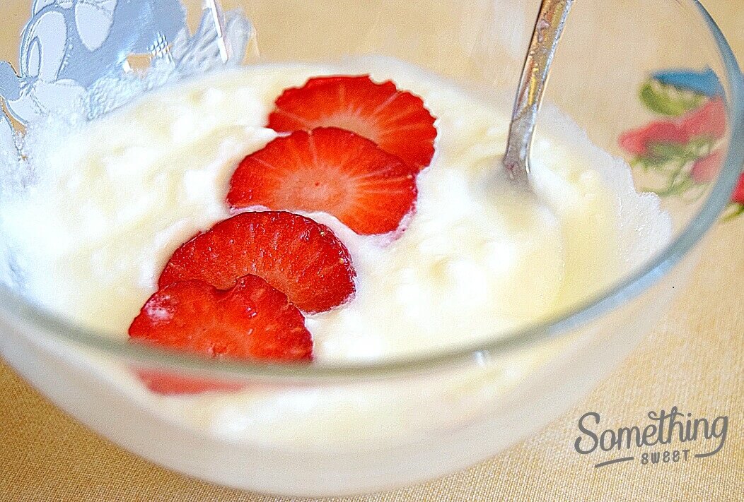 yogur con cachitos de fresas en un cuenco de vidrio junto a cuchara