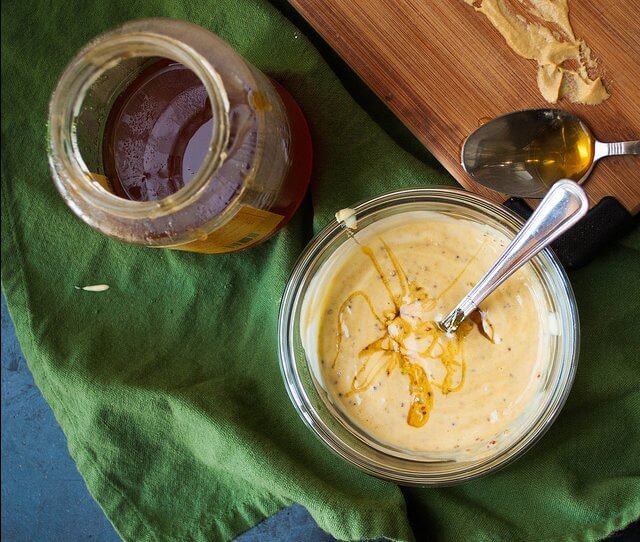 un bote con salsa de miel y mostaza junto a una cuchara